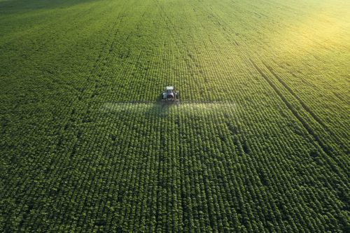 aerial shot tractor spreading herbicides over field