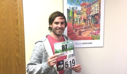 A man smiling and holding two race bibs in front of himself.