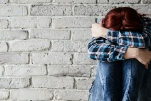 woman sitting against brick wall while hugging her knees with her head down