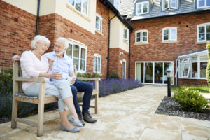 Retired Couple Sitting On Bench With Hot Drink In Assisted Living Facility