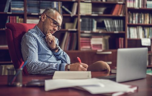 man-works-in-academic-office-with-bookshelves-and-desk