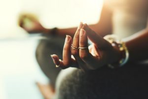 Close-up of a woman in a seated meditation with her hands resting on her knees, legs crossed.