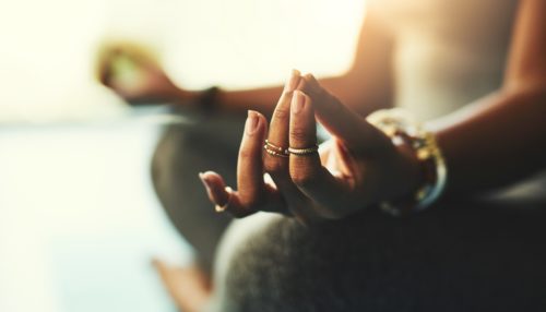 Close-up of a woman in a seated meditation with her hands resting on her knees, legs crossed.